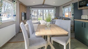 A cozy living room with a wooden dining table, grey upholstered chairs, a sofa, and a kitchen area with a microwave and cabinets. - South Beach Landings 0028 (Rye)