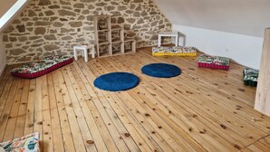 Une pièce mansardée chaleureuse avec un plafond en pente, un mur en pierre, un plancher en bois et plusieurs coussins aux couleurs vives.
