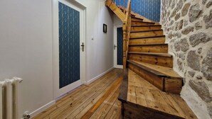 Un escalier en bois, avec un mur de pierre d’un côté et une porte recouverte d’un papier peint à motifs bleus de l’autre.