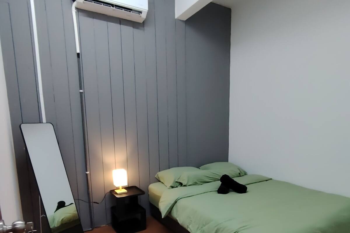 Una habitación con una cama, una mesita de noche con lámpara, un espejo y un equipo de aire acondicionado.