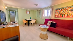 Ein Wohnzimmer mit einem roten Sofa, einem Esstisch mit Stühlen, einem Fernseher und einem Bild an der Wand.