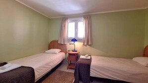 Ein Zimmer mit zwei Einzelbetten, einem kleinen Tisch mit Lampe und einem fenster mit Vorhängen.