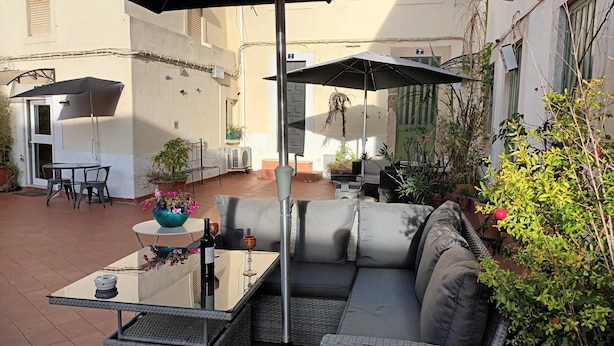 Eine Außenpatio mit einer Couch, einem Tisch und Stühlen, umgeben von Topfpflanzen und einer Pergola.