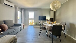 Una sala de estar moderna con un sofá gris, una mesa de comedor con desayuno servido y un televisor montado en la pared.