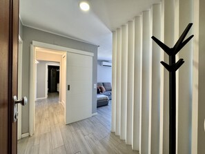 Ein Flur mit einer zur Kammer führenden Tür, einem Kleiderhaken und einem Bett mit Kissen.