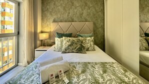 Habitación de hotel con cama, mesita de noche, lámpara y vistas a edificios a través de una ventana.