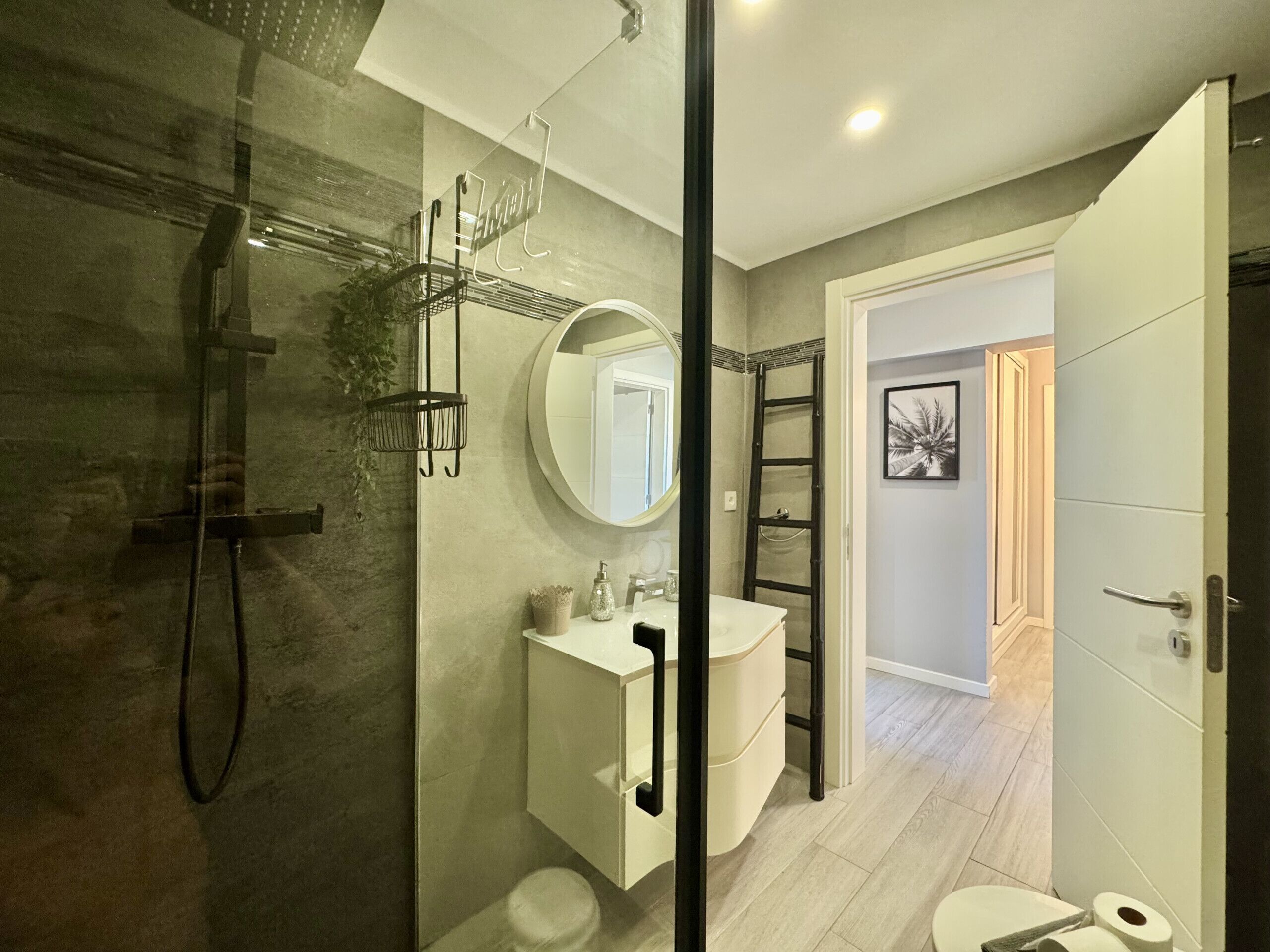 A modern bathroom with a glass-enclosed shower, a round mirror, a white sink, and a toilet.