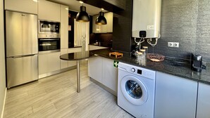 Et moderne køkken med stålemmer, indbygget ovn, mikroovn, vaskemaskine og kaffemaskine.