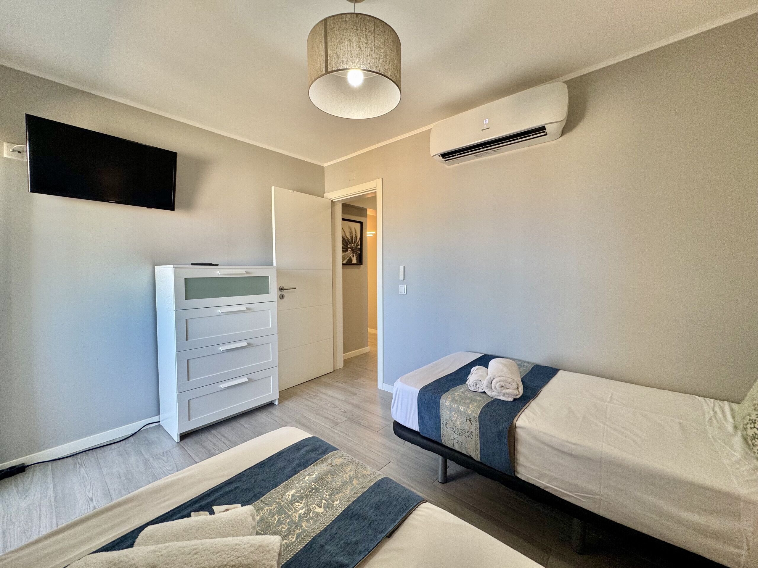 A hotel room with a bed, a wardrobe, a television, and an air conditioning unit.