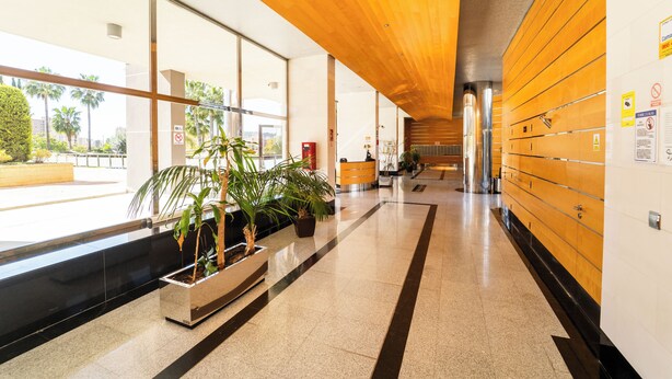 A modern hotel lobby with a wooden ceiling, large windows, and a reception desk.