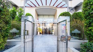 The entrance to a hotel with a modern design, featuring a glass facade and a sign reading "TORRE DOSCALAS".