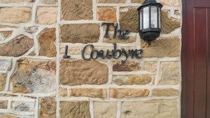 A stone wall with a sign reading "The 1 Coubyre" and a black lantern. - The Cow Byre (Saltburn-by-the-Sea)
