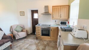 A compact kitchen with wooden cabinets, a microwave, a toaster, and a washing machine. - The Cow Byre (Saltburn-by-the-Sea)