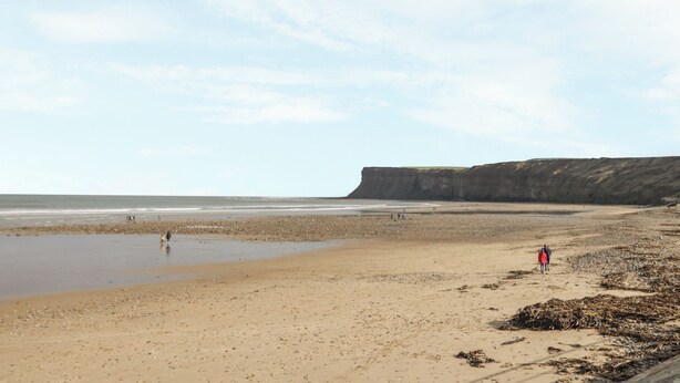 A wide sandy beach with a cliff in the background. - The Cow Byre (Saltburn-by-the-Sea)