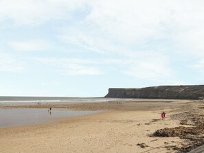 A wide sandy beach with a cliff in the background. - The Cow Byre (Saltburn-by-the-Sea)