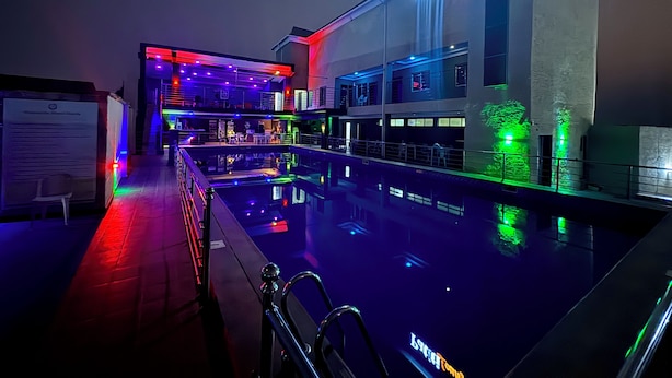 Area piscina con bar e zona relax, un cartello con scritto 'Patio Lounge' e una piscina che riflette l'ambiente circostante.