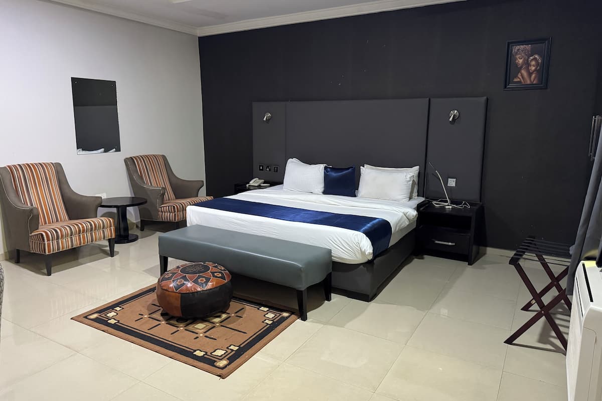 Een moderne hotelkamer met een groot bed, twee fauteuils, een klein tafeltje en een nachtkastje met een lamp.