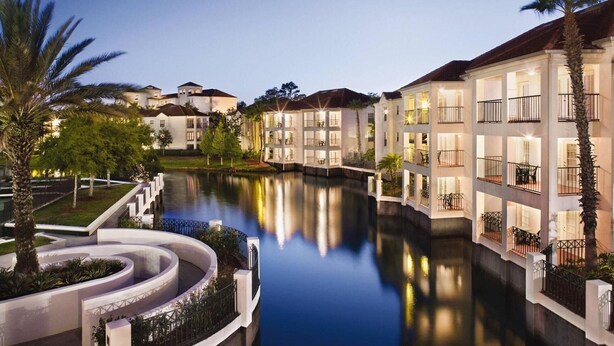 Un hotel sul canale con numerosi balconi, uno specchio d'acqua e giardini curati.