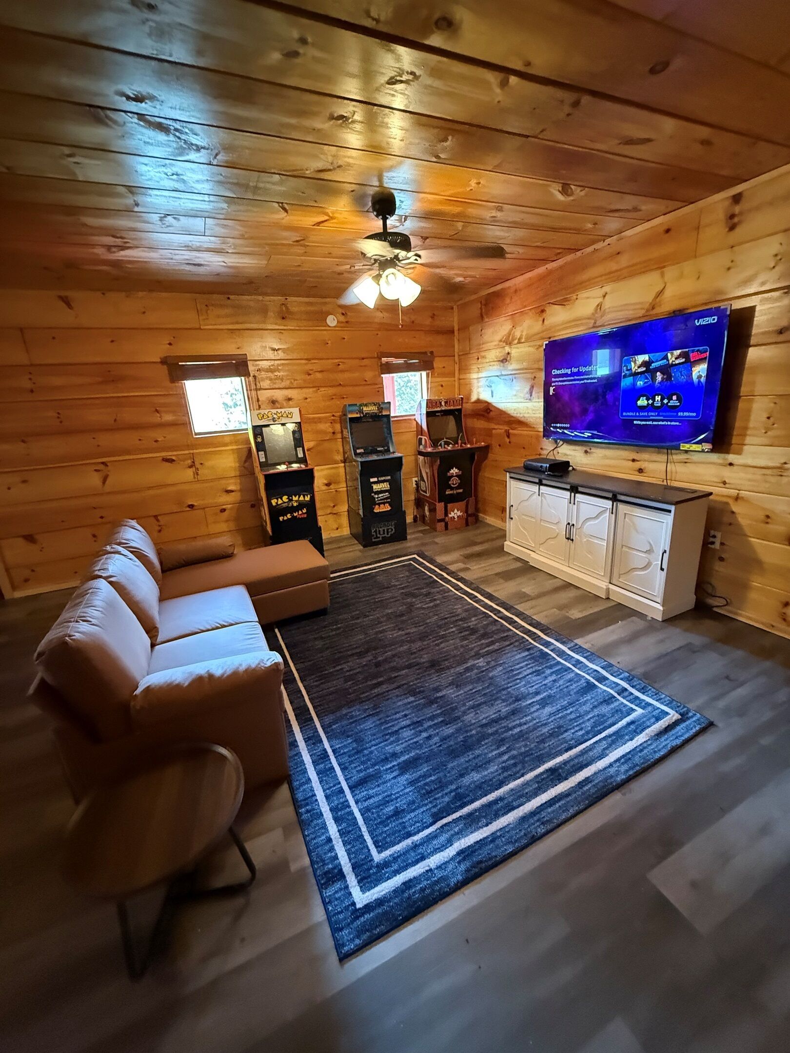 Une pièce chaleureuse avec un décor intérieur en bois, un canapé en cuir, un téléviseur et deux bornes d’arcade.