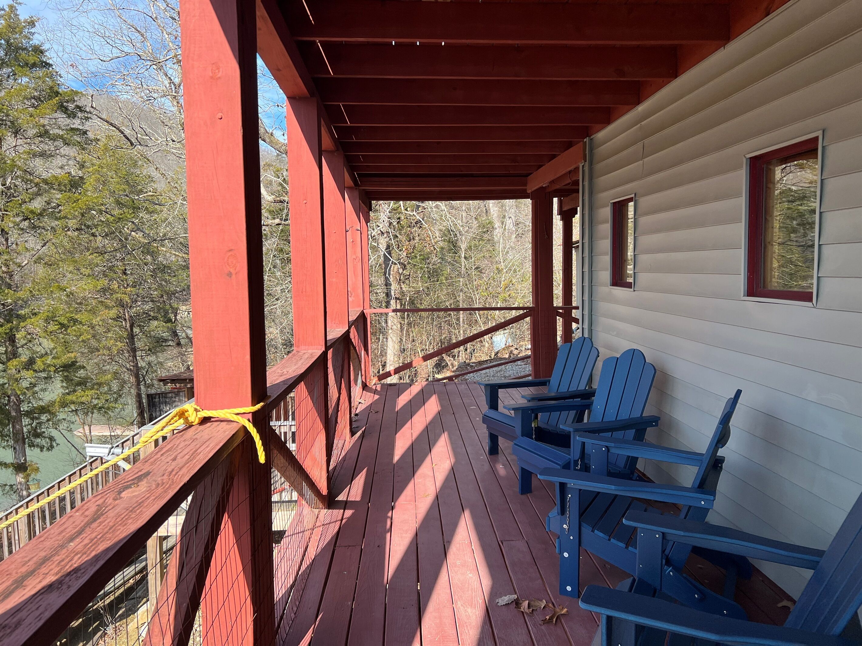 A wooden deck with red railings, two blue Adirondack chairs, and a white cabin with a window.