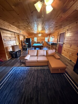 L'intérieur d'un chalet confortable, avec un canapé, une table de billard et des murs en bois.