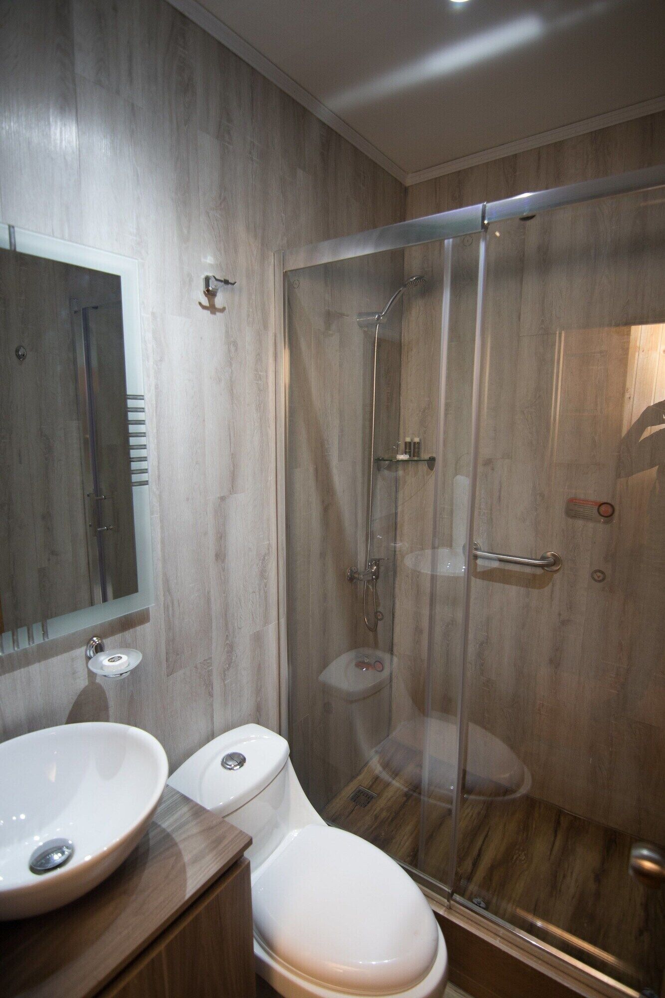 Un baño moderno con ducha envuelta en vidrio, tocador de madera y un espejo grande.