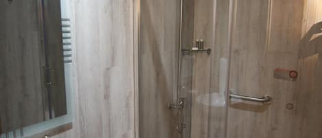 Un baño moderno con ducha envuelta en vidrio, tocador de madera y un espejo grande.
