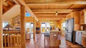 A log cabin interior with a kitchen, dining area, and a stone fireplace. - Charming Log Cabin + Mountain Views + Fireplace + Hot Tub + Pet Friendly (Cripple Creek)