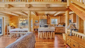 A log cabin interior with a wooden dining table, bar stools, a kitchen with wooden cabinets, and a staircase. - Charming Log Cabin + Mountain Views + Fireplace + Hot Tub + Pet Friendly (Cripple Creek)