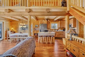 A log cabin interior with a wooden dining table, bar stools, a kitchen with wooden cabinets, and a staircase. - Charming Log Cabin + Mountain Views + Fireplace + Hot Tub + Pet Friendly (Cripple Creek)