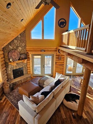 Ein gemütliches Blockhaus-Interieur mit Kamin aus Stein, einem großen Holzdeckenventilator und einem Hundebett.