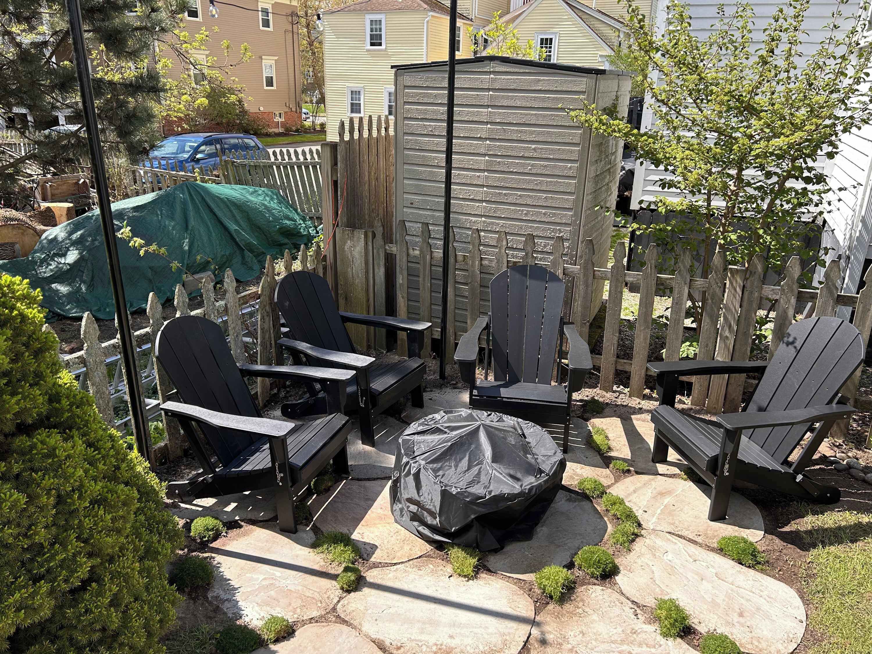 Eine Terrasse mit Adirondack-Stühlen, einem überdachten Grill und einem Holzzaun.