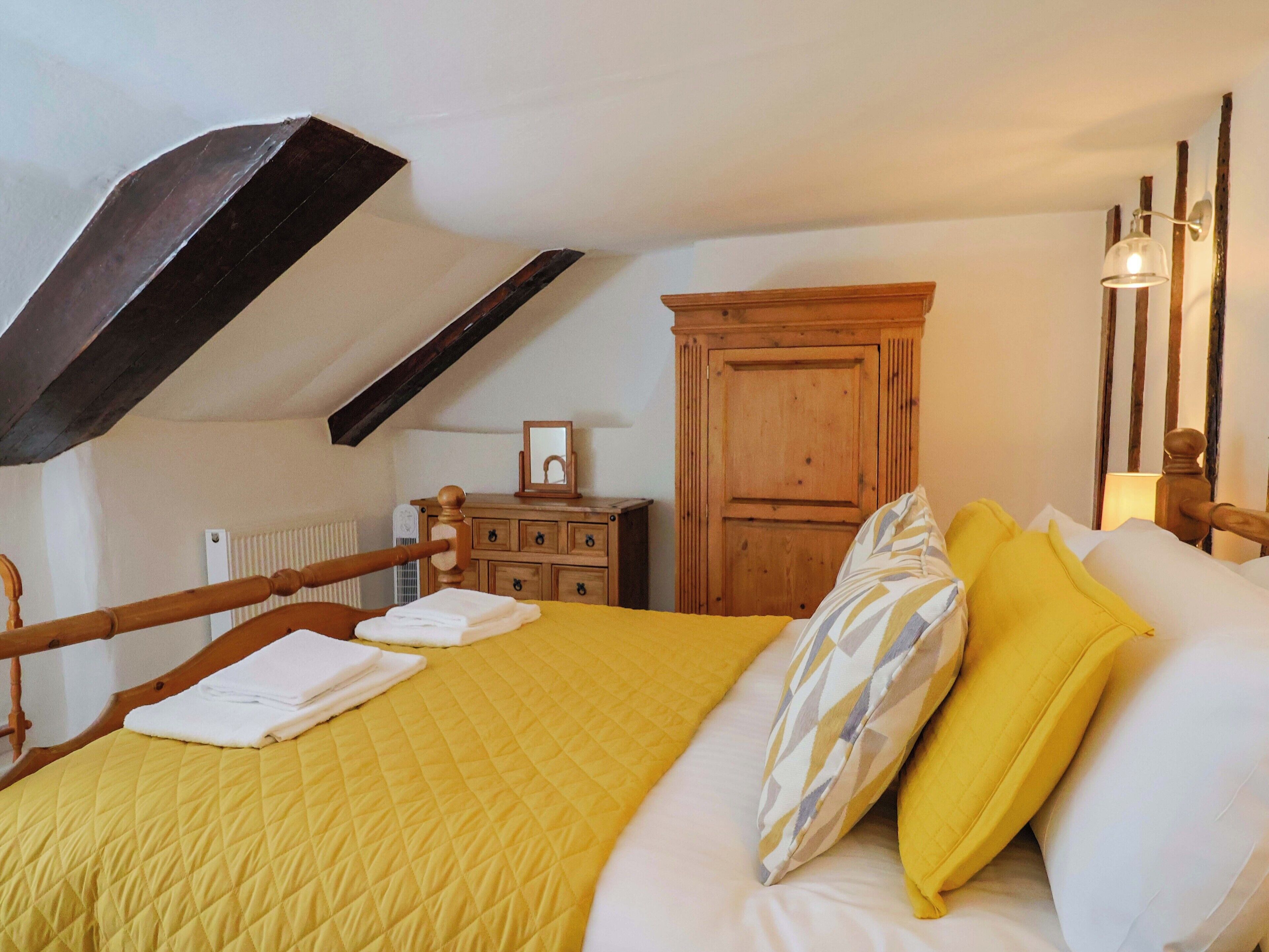 A bedroom with a bed, wooden dresser, and a sloped ceiling.