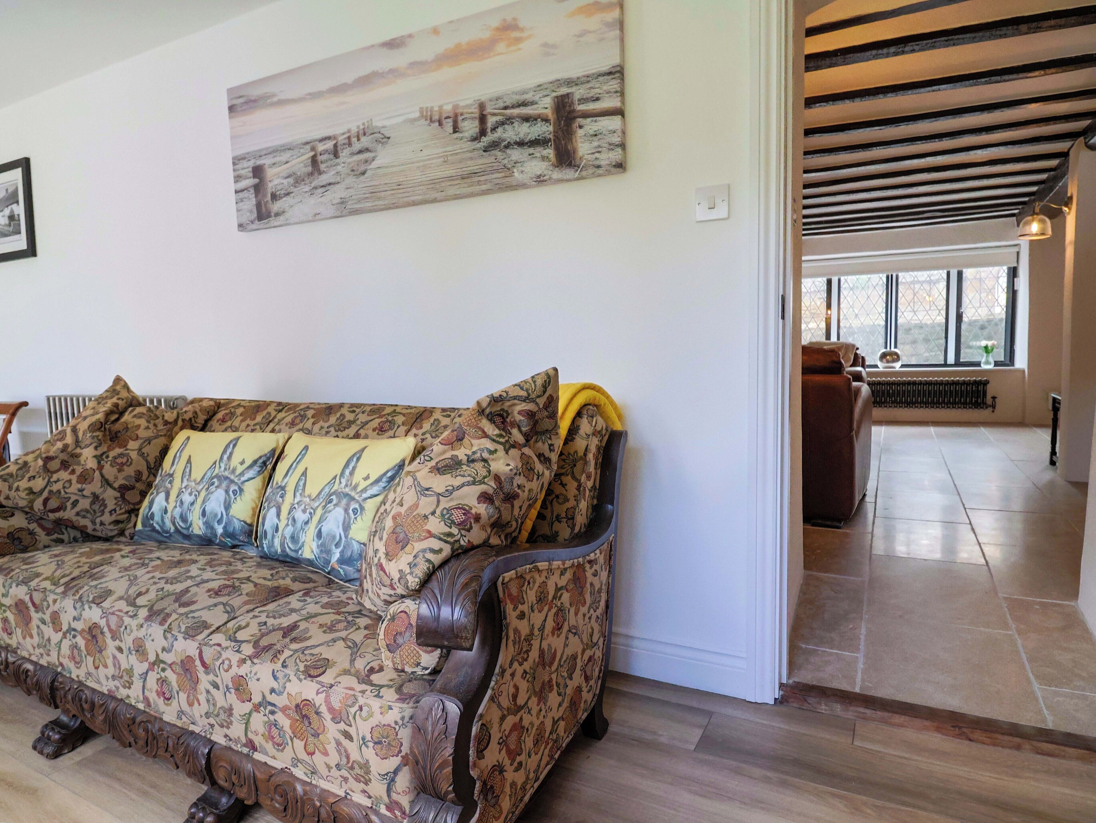 A living room with a patterned sofa, a painting on the wall, and a view into another room.