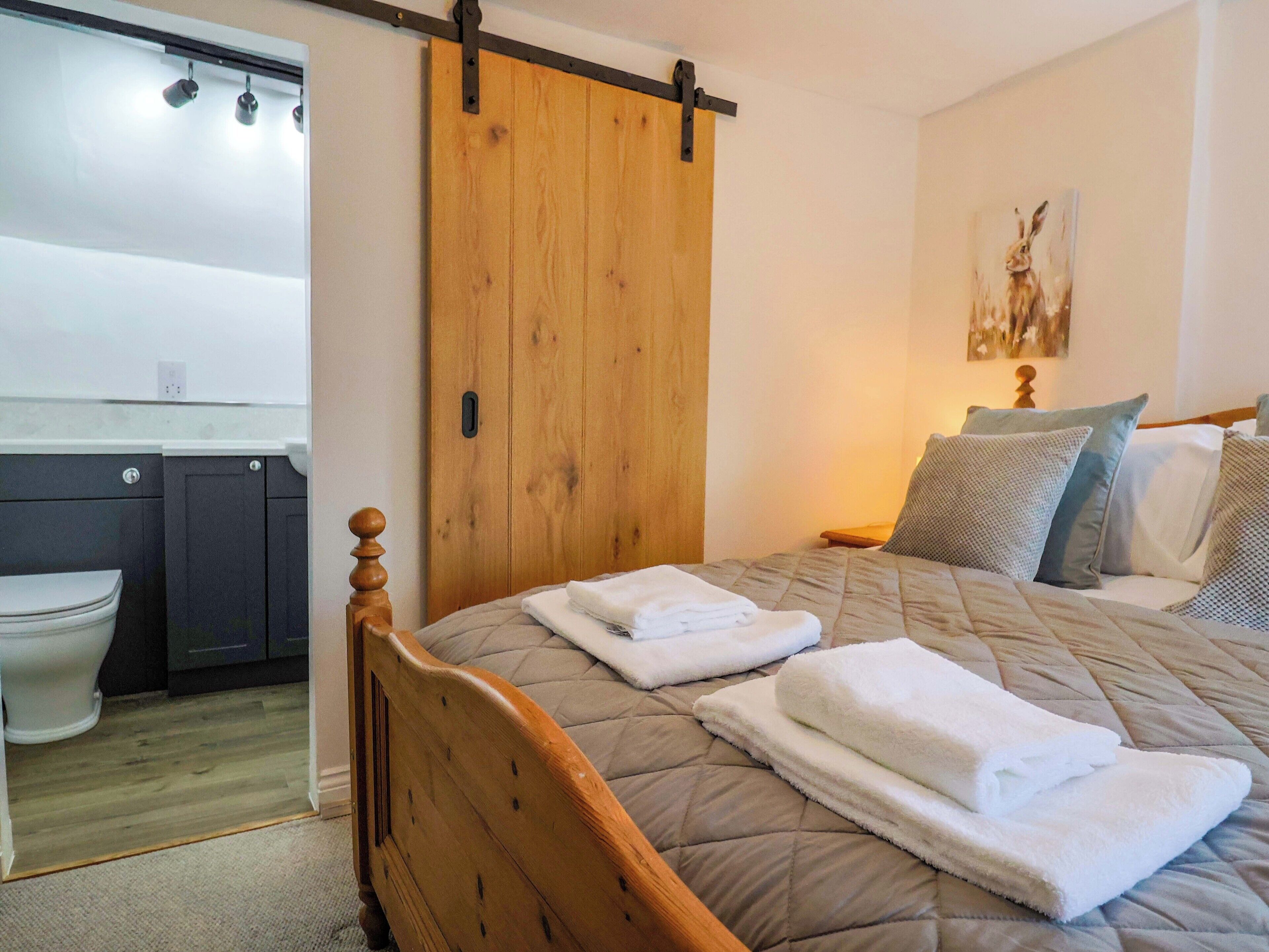 A bedroom with a wooden bed, a sliding door, a bathroom with a toilet, and a painting on the wall.