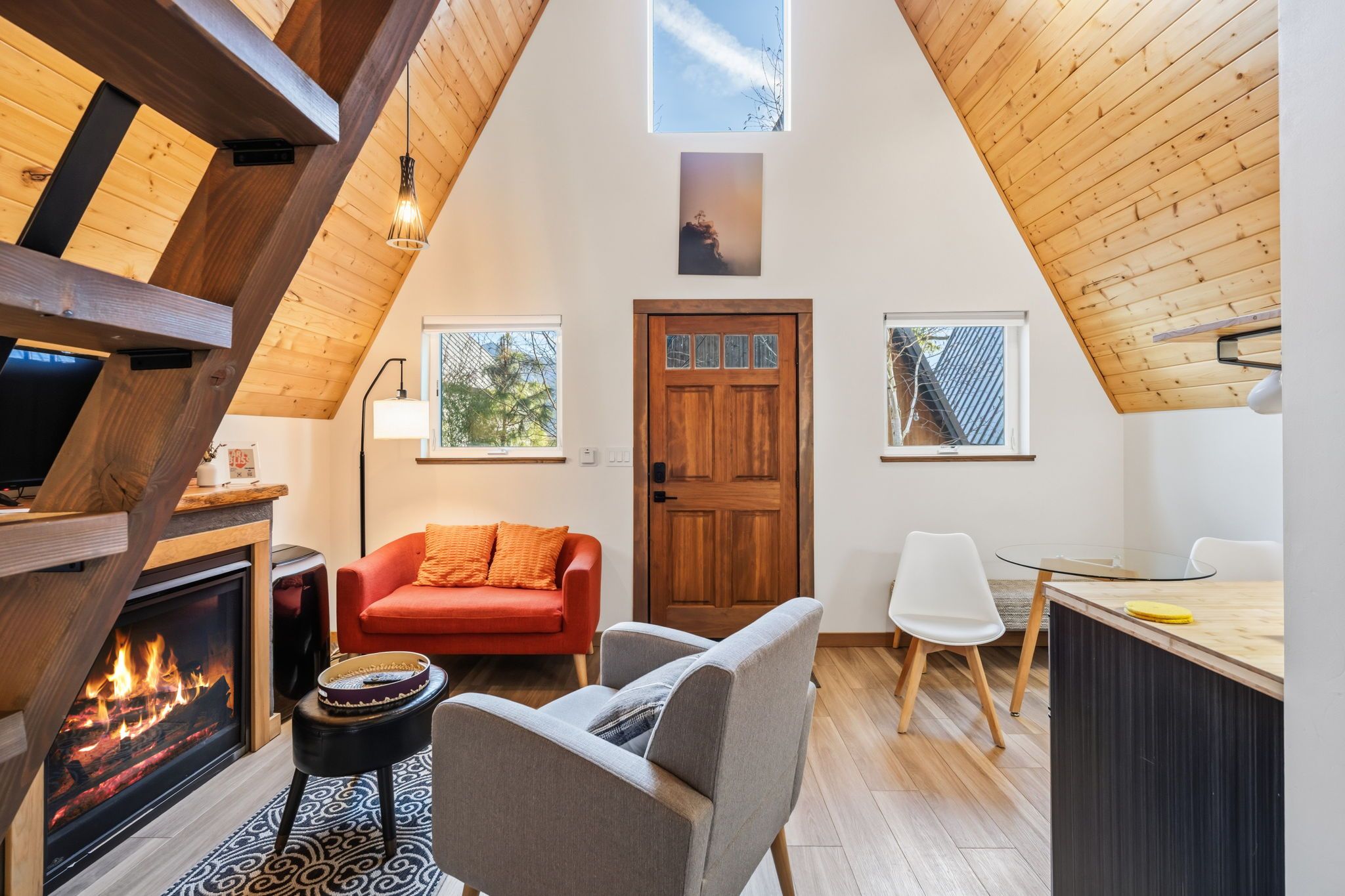 Un ambiente acogedor con chimenea, un sofá rojo, una zona de comedor y techo de madera.