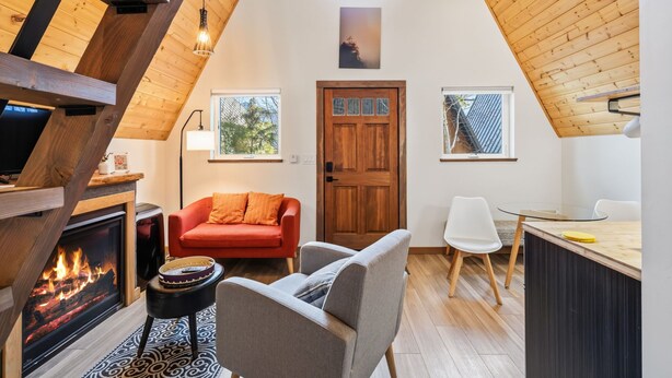 Een gezellig interieur met een open haard, een rode bank, een eethoek en een houten plafond.