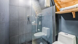 Een moderne badkamer met een glazen douchecabine, een toilet en een houten plank met handdoeken.