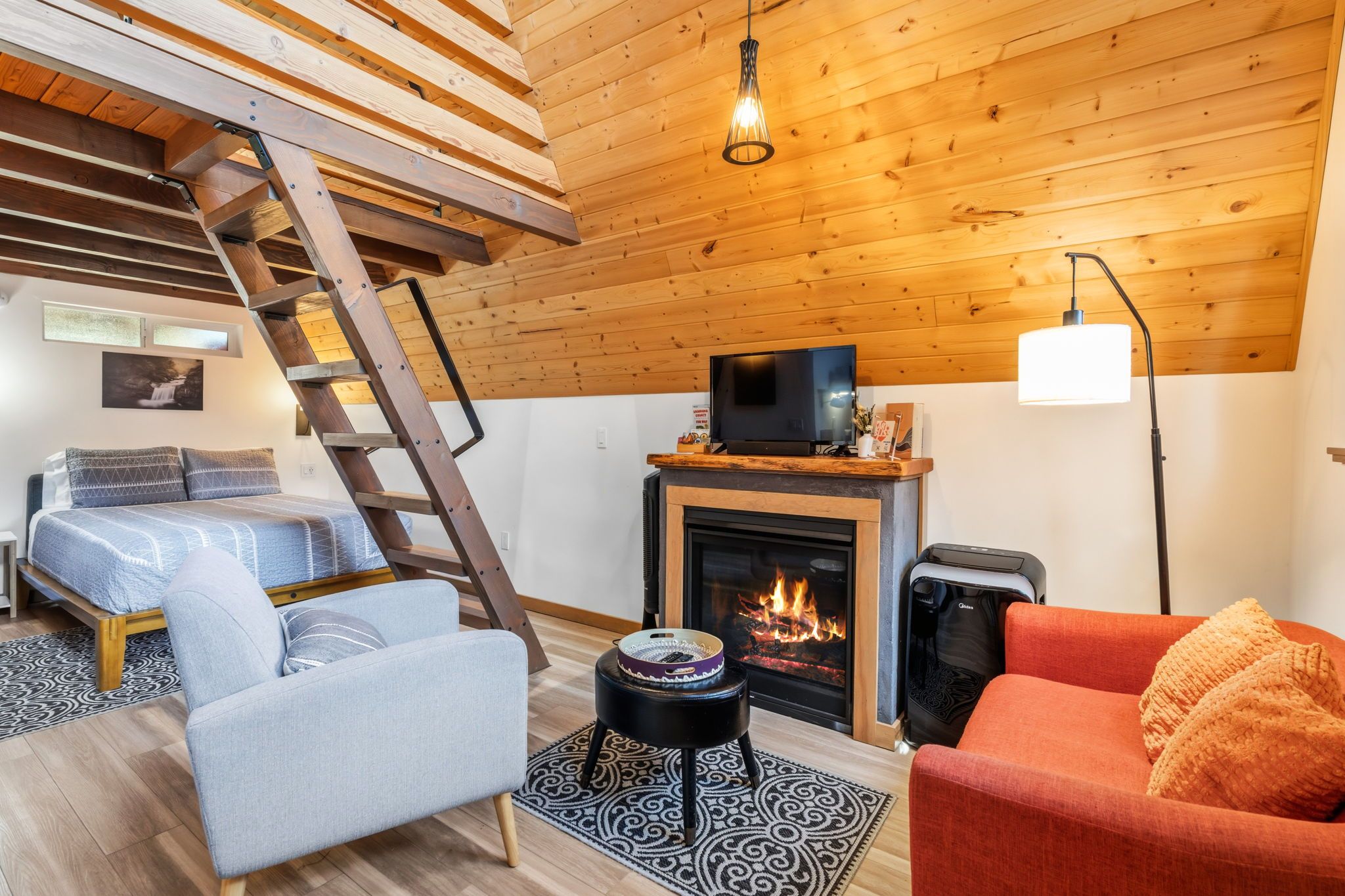 Una sala de estar acogedora con chimenea, televisor, sofá, sillón, una escalera y una alfombra estampada.