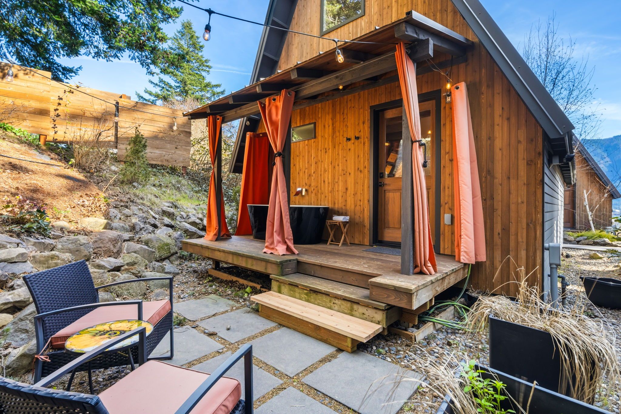 Una cabaña de madera con porche, escalones de piedra y mobiliario exterior.