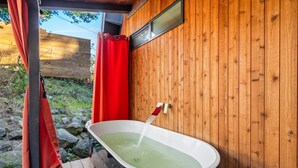 Een houten chalet met een jacuzzi, een rood gordijn en een houten terras.