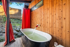 Een houten chalet met een jacuzzi, een rood gordijn en een houten terras.