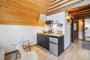 Una cocina compacta con vigas de madera en el techo, un microondas, un lavamanos y un refrigerador.