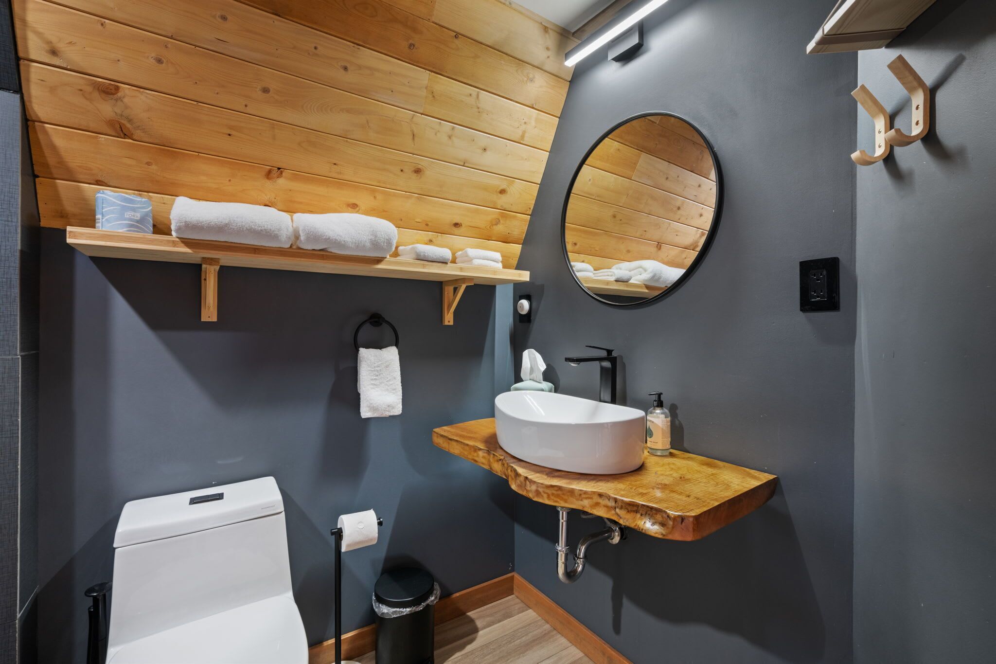 Un baño moderno con tocador de madera, un espejo redondo y un inodoro.