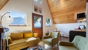 Uma sala de estar acolhedora com sofá, poltronas, uma mesinha e um espaço de cozinha com televisão e micro-ondas.