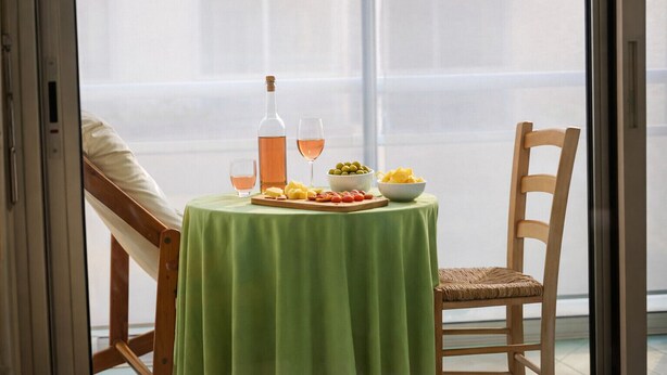 Una mesa de comedor con mantel verde, una botella de vino, copas y fuentes de comida.
