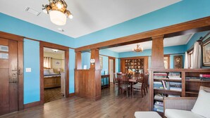 A spacious living room with wooden flooring, a dining area with a wooden table and chairs, and a bookshelf filled with books. - Historic Prescott Craftsman | Walk Downtown (Prescott)
