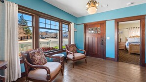 A room with wooden flooring, two upholstered chairs with floral cushions, a chandelier, and a view of a mountain through large windows. - Historic Prescott Craftsman | Walk Downtown (Prescott)