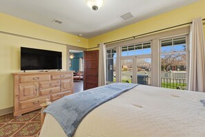 Un dormitorio con cama, cómoda, televisor y puerta corrediza de vidrio que da a un balcón.