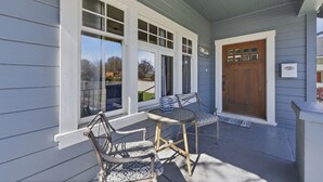 A covered porch with a table and chairs, a wooden door, and large windows. - Historic Prescott Craftsman | Walk Downtown (Prescott)